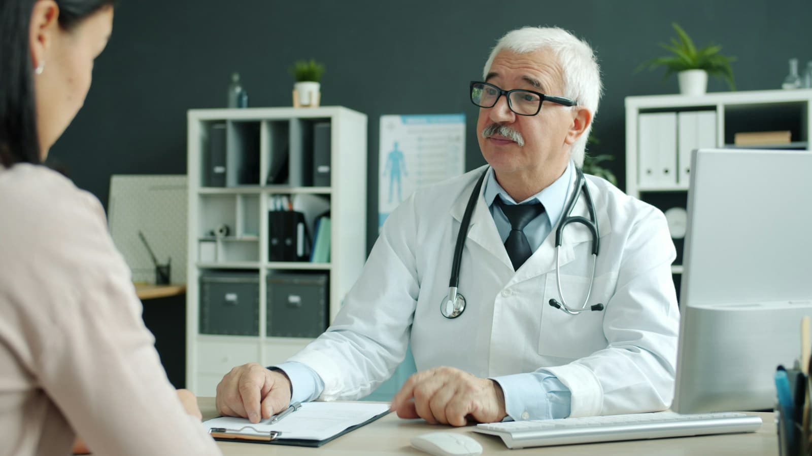 A doctor with a stethoscope talking with a visitor across a desk in a clinic office